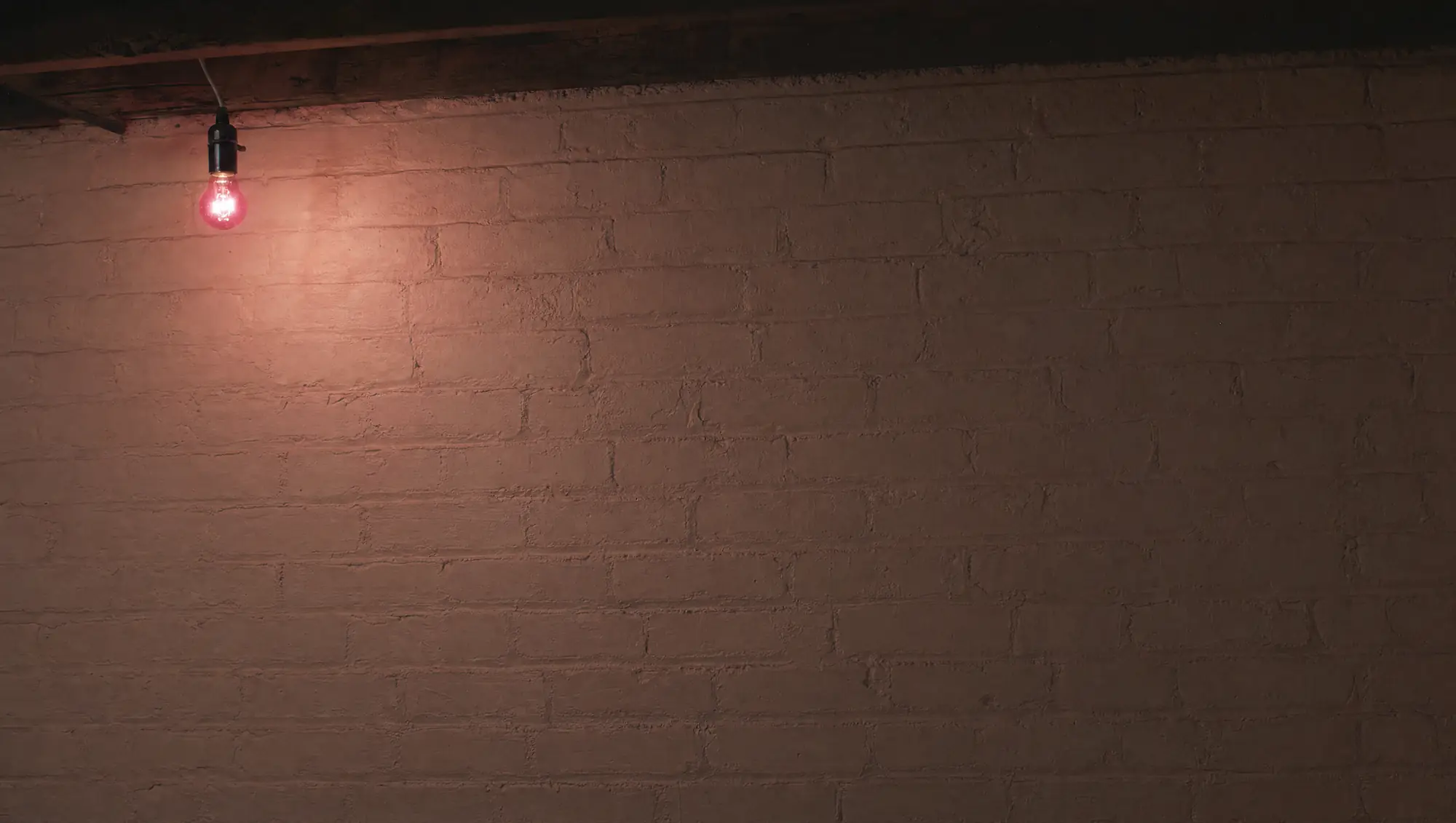 A painted brick wall in a basement, one red bulb on a wire.